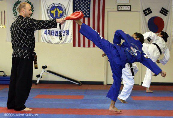 A student in a blue uniform kicks a target held by an instructor. © 2006 Allen Sullivan.