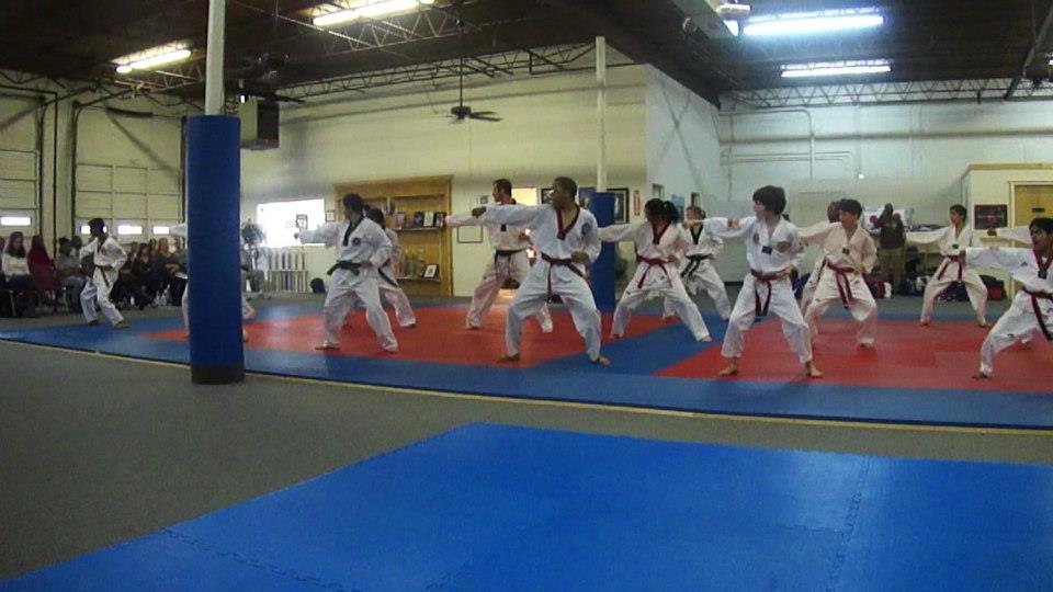 Students in white uniforms practice in a line across the mats.
